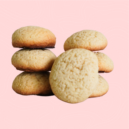 A stack of soft, sugar-free vanilla cookies with a light golden hue, set against a soft pink background. A simple, timeless flavor made for guilt-free enjoyment