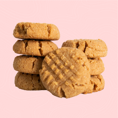 A stack of soft, golden-brown sugar-free peanut butter cookies with a signature crisscross pattern, set against a light pink background. Perfectly rich and nutty for a guilt-free peanut butter treat