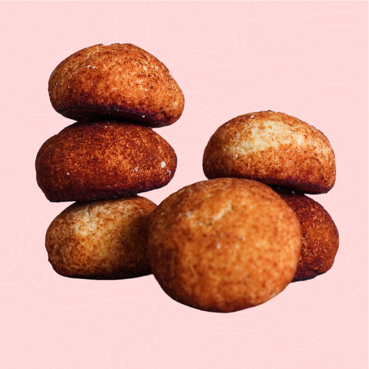 A stack of sugar-free snickerdoodle cookies, perfectly golden with a cinnamon-sugar coating, set against a soft pink background. A warm, classic flavor reimagined for guilt-free enjoyment.