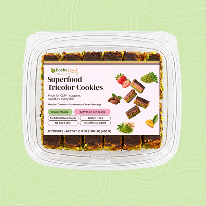 BochaSweet Superfood Tricolor Cookies, 12 layered chocolate-topped cookies in a clear clamshell on a light green background. The label highlights 5 superfoods (matcha, turmeric, strawberry, cacao, and moringa), 6g protein per cookie, no added cane sugar, and gluten-free.